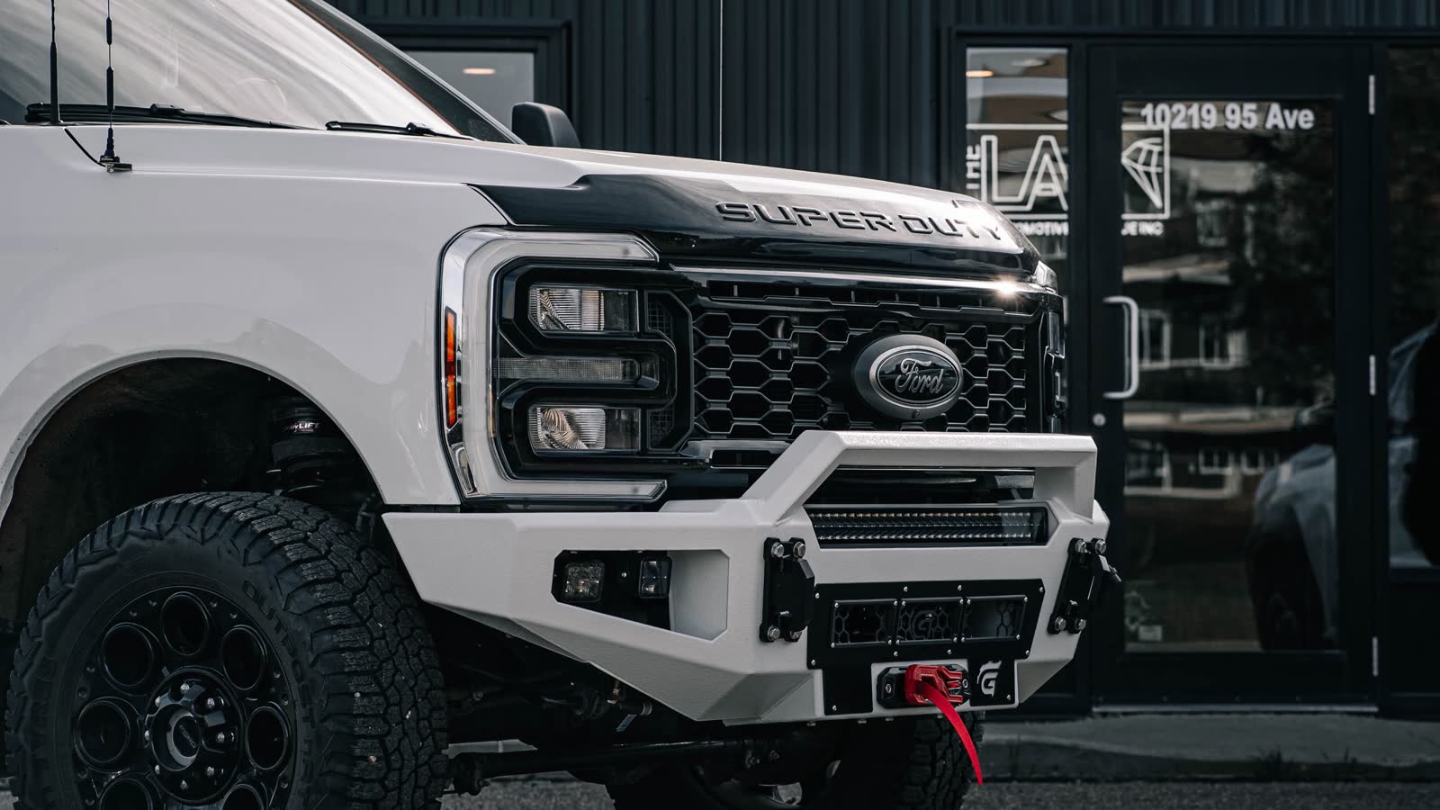 White Ford Super Duty with a Gridiron steel bumper, winch and LED light bar parked outside THE LAB shop